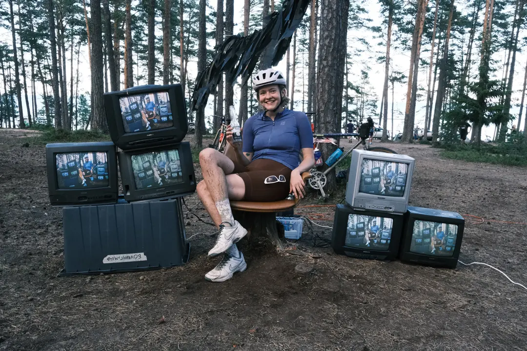A member of FURY ROAD sits next to TVs in a forest camp