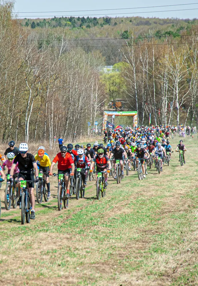 A large group of MVM participants is riding through a field near the forest.