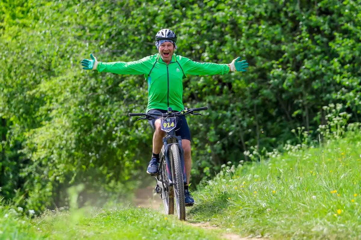 The participant of the bike marathon with the number 914 rides along the green forest highway